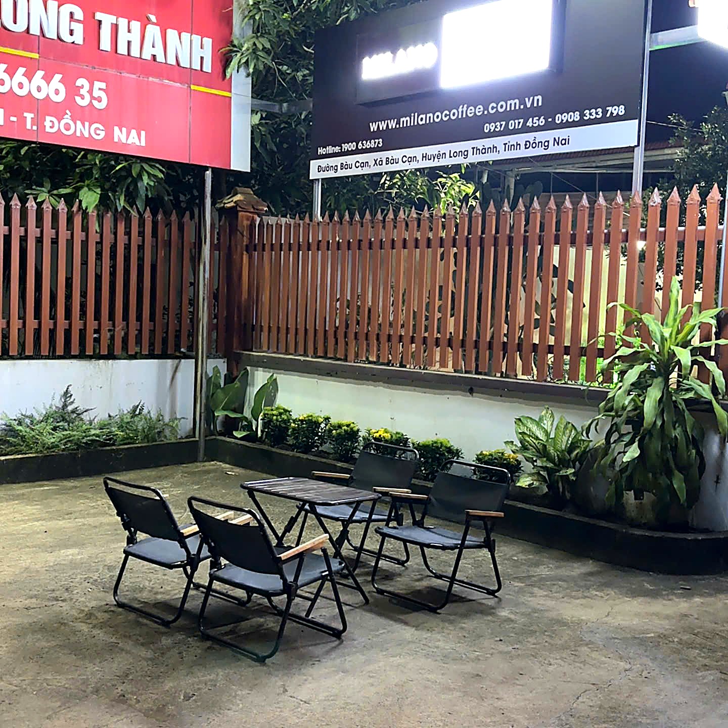 Bảng hiệu Milano Coffee sáng đèn buổi tối bên khu bàn ghế sân trước